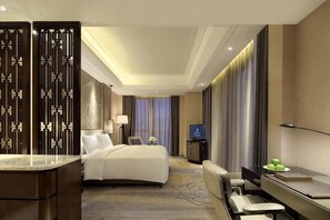 A hotel room with a bed, desk, chair, and a TV.