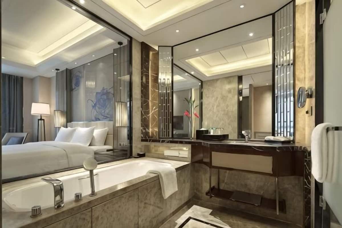 A modern hotel bathroom with a large mirror, a bathtub, a vanity with a sink, and a separate shower area.