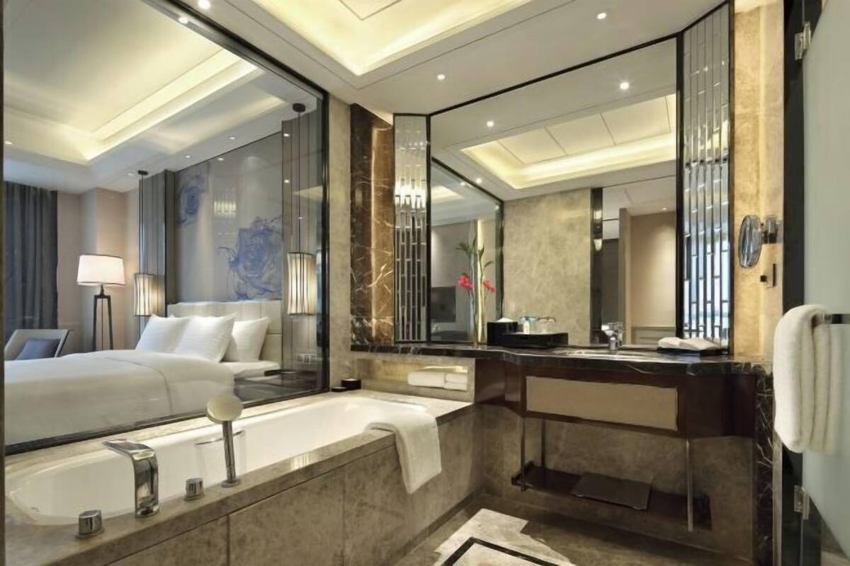 A modern hotel room with a large bed, a bathtub, a vanity with a mirror, and a large mirror reflecting the room.