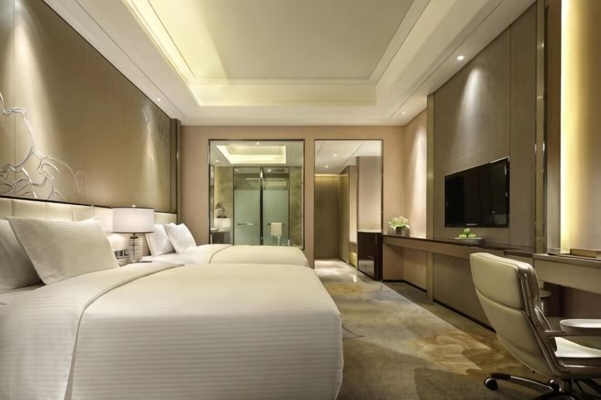 A hotel room with a large bed, a desk, a chair, a television, and a mirror.