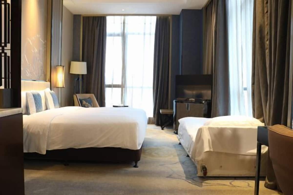 A hotel room with two beds, a TV, a desk, and a lamp.