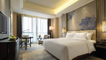 A hotel room with a large bed, a desk with a chair, a TV, and a view of the outdoors.