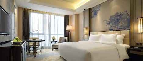 A hotel room with a large bed, a desk with a chair, a TV, and a view of the outdoors.