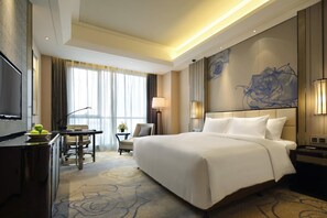 A hotel room with a large bed, a desk with a chair, a TV, and a view of the outdoors. - Wanda Realm Fuyang (Fuyang)