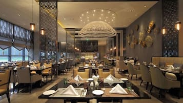 Ein modernes Restaurant mit mehreren Tischen und Stühlen, einem dekorativen Kronleuchter und Blick ins Freie.