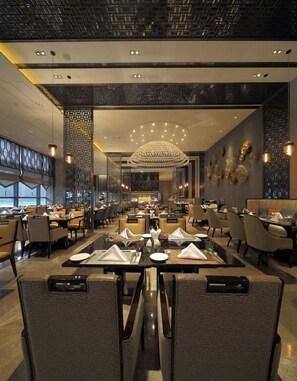 A modern restaurant with multiple dining tables and chairs, a decorative chandelier, and a view of the outside. - Wanda Realm Fuyang (Fuyang)