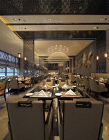 Un restaurante moderno con varias mesas y sillas para comer, un candelabro decorativo y vistas al exterior.
