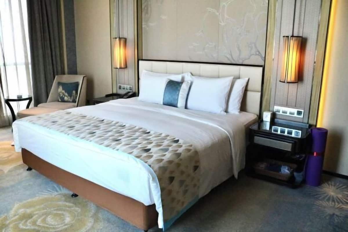 A hotel room with a large bed, nightstands, a chair, and a wall-mounted lamp.