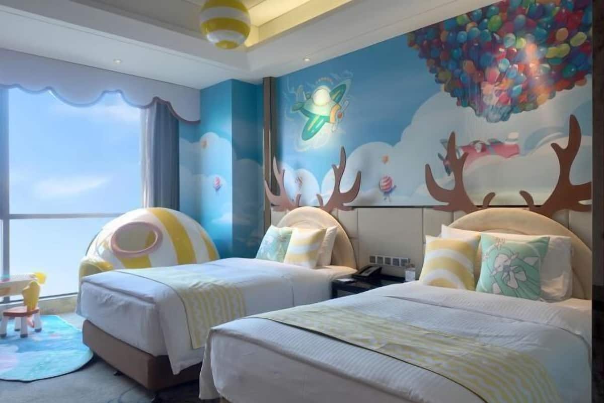 A hotel room with two beds, a large window, and a mural with a flying saucer and reindeer.