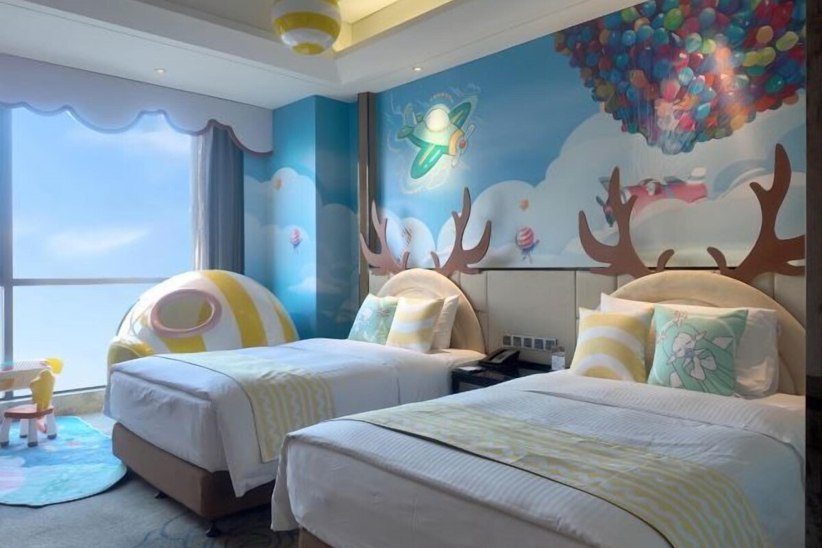 A hotel room with two beds, a large window, and a mural with a flying saucer and reindeer.