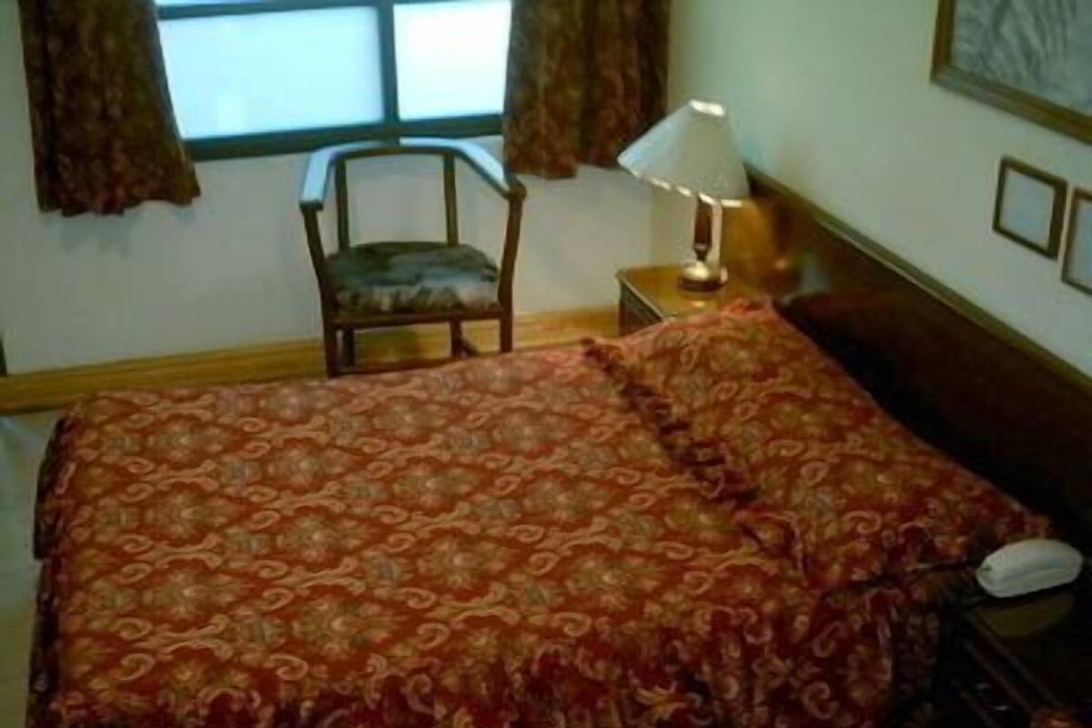 Un dormitorio con una cama grande, una silla, una mesita de noche, una lámpara y un cuadro en la pared.