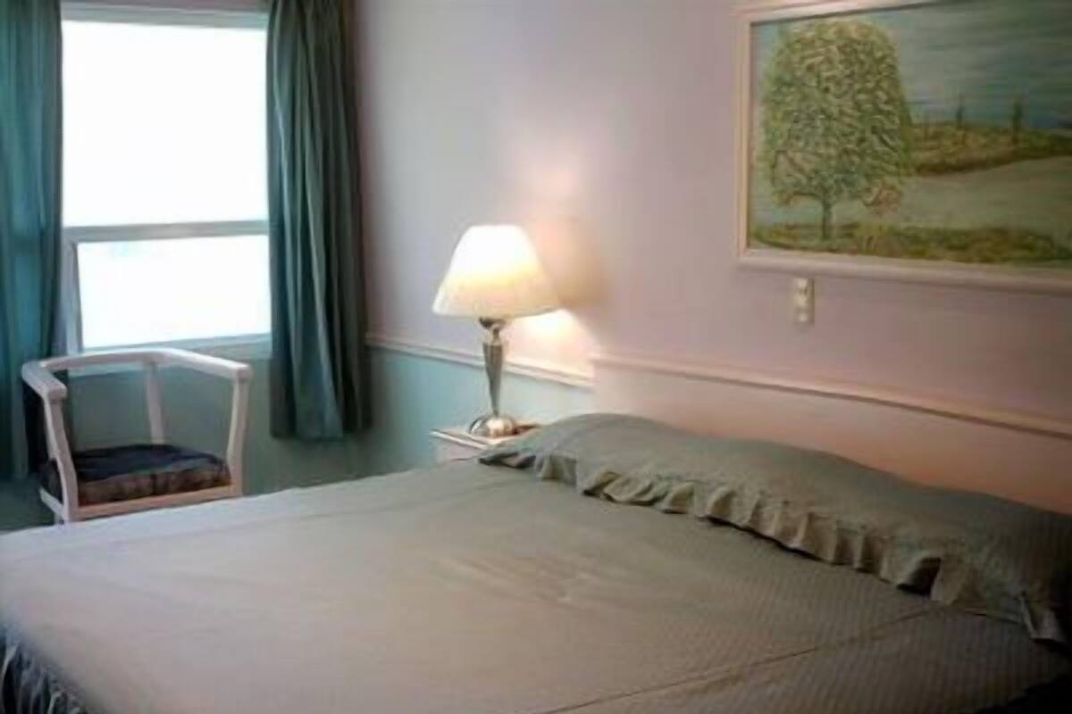 Un dormitorio con cama, una silla, una lámpara y un cuadro en la pared.