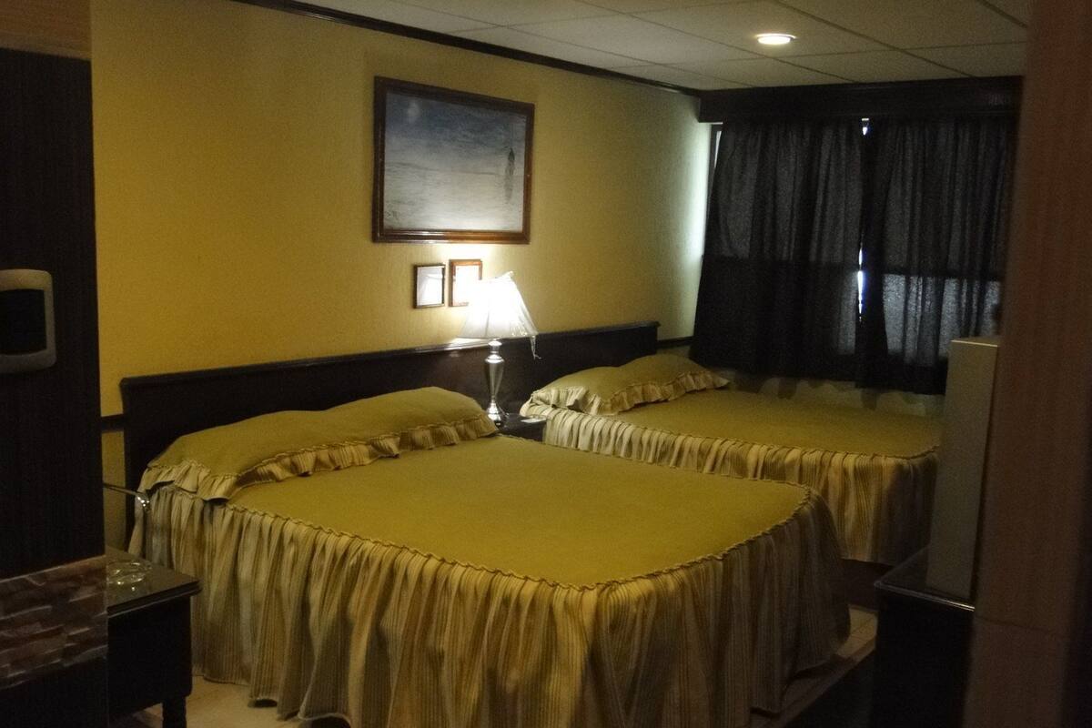 Una habitación de hotel con dos camas, una mesita de noche, una lámpara y un cuadro en la pared.