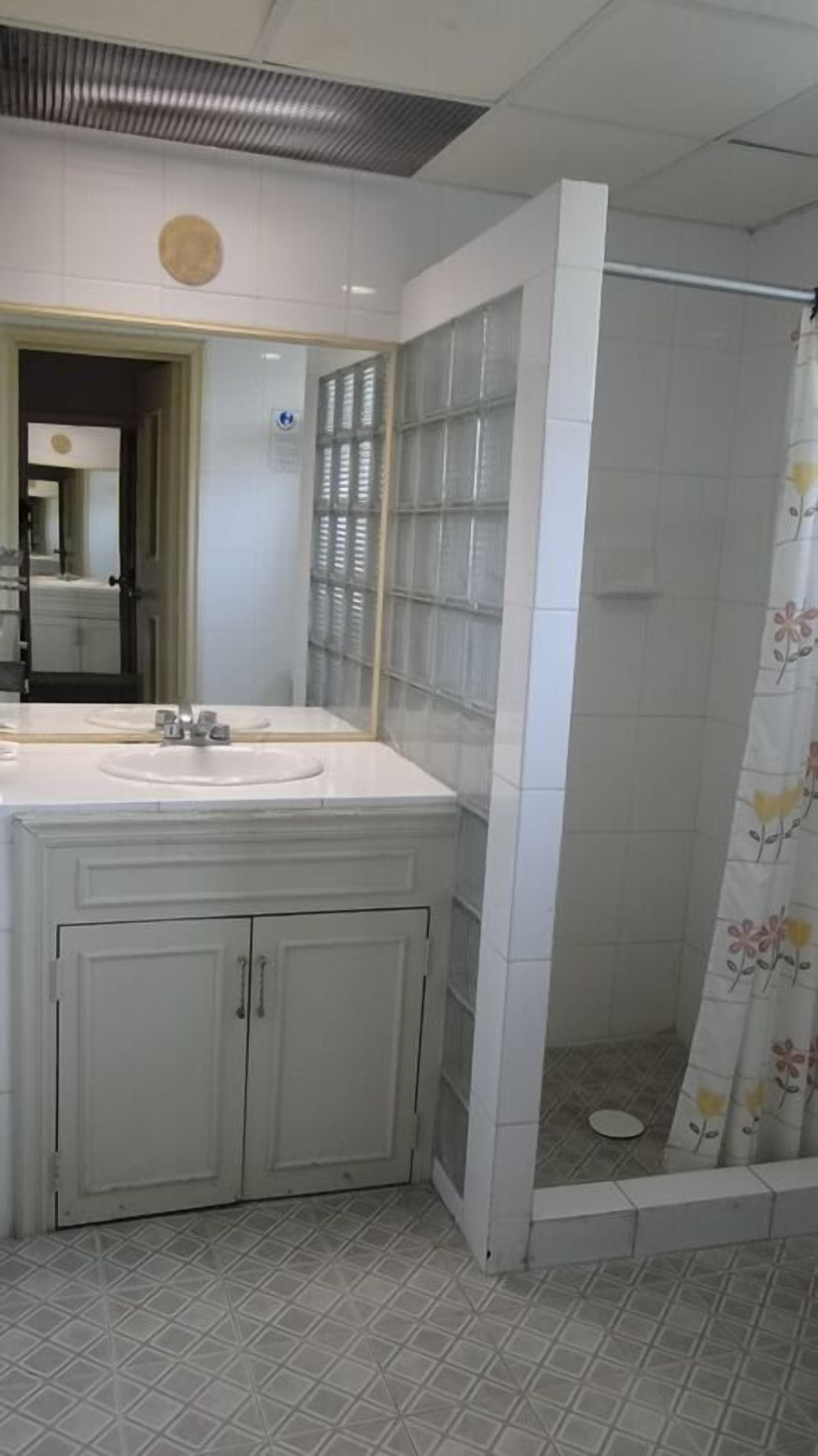 Un baño con tocador blanco, ducha con cortina estampada y suelo de baldosas.