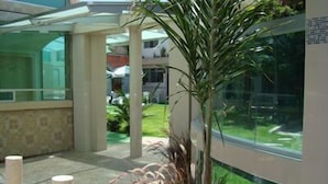 A modern building with a glass facade, a covered outdoor area with plants, and a view of a green landscape. - Hotel Cuellar (Tula de Allende)