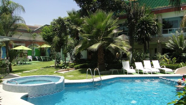 A swimming pool with lounge chairs, a hot tub, and lush greenery. - Hotel Cuellar (Tula de Allende)