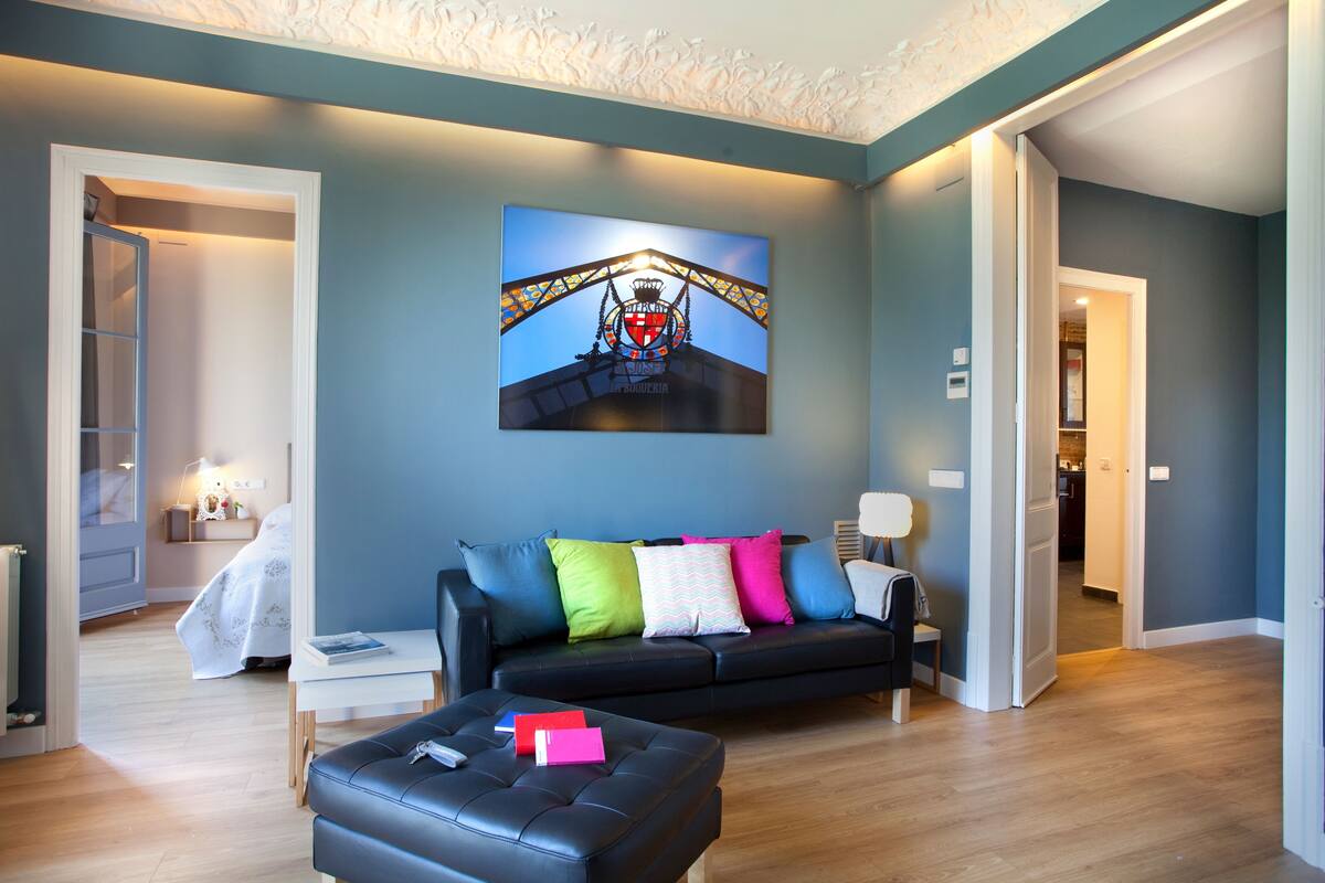 A modern living room with a black sofa, colorful cushions, a coffee table, and a framed picture on the wall.