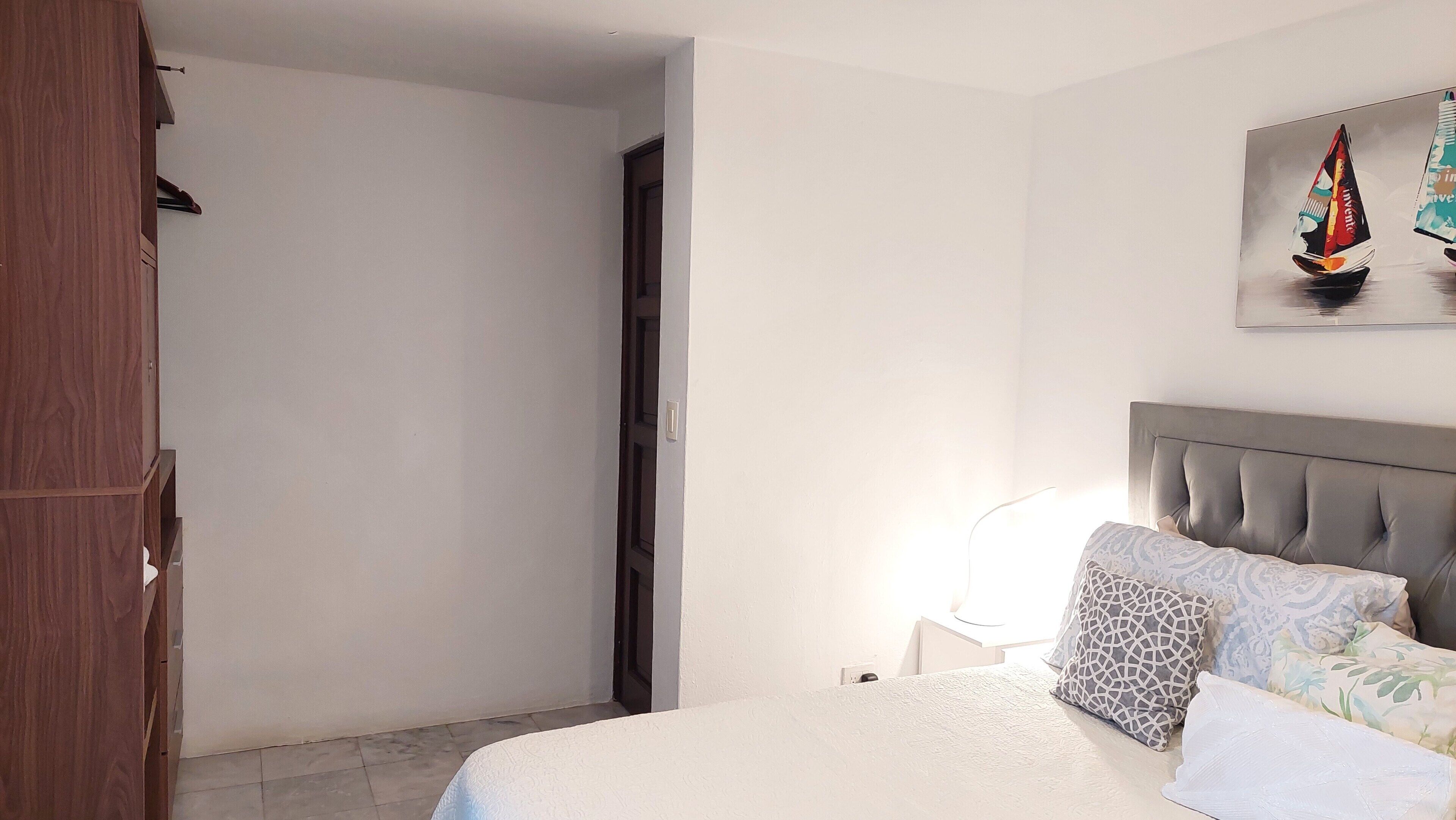 Een slaapkamer met een bed, nachtkastje, lamp en een schilderij van een zeilboot.