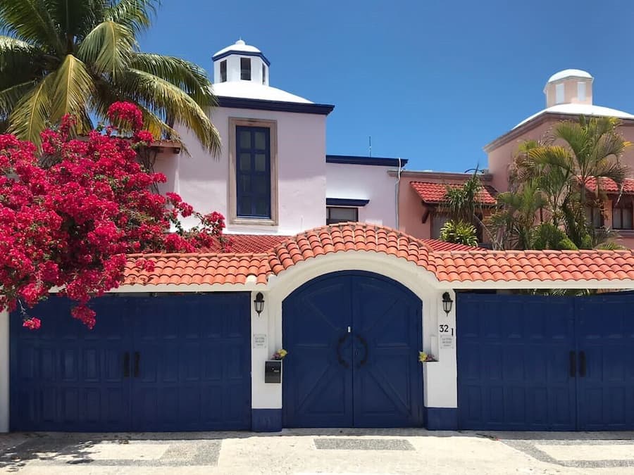 Un edificio con fachada blanca, techo de tejas rojas y puerta de garaje azul.