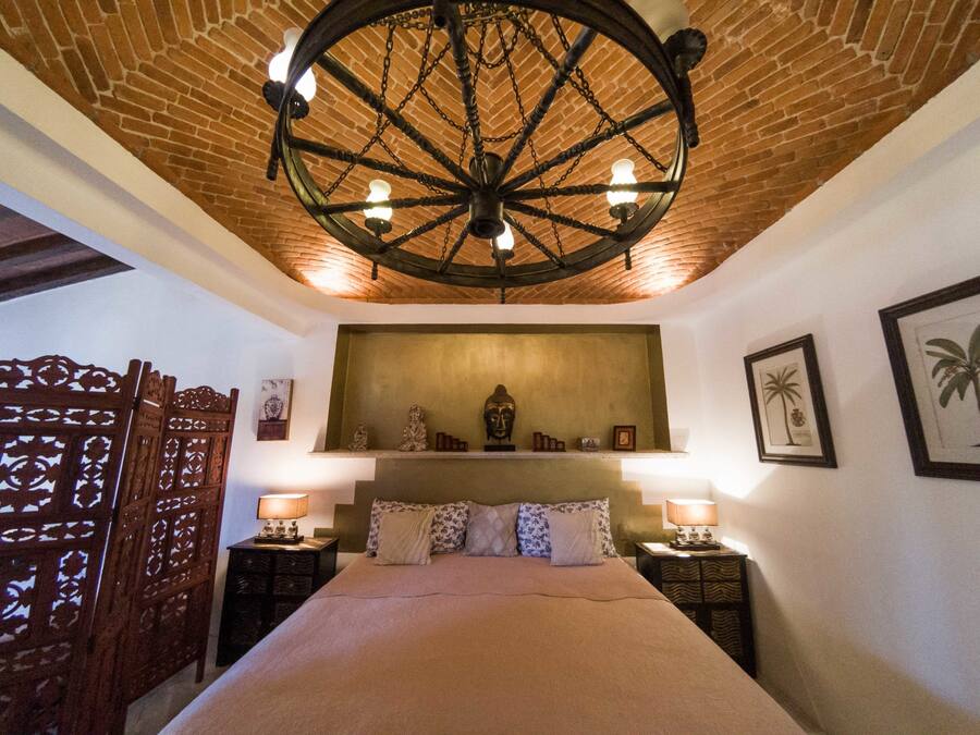 A room with a large bed, a wooden ceiling, and a wall-mounted shelf with decorative items.