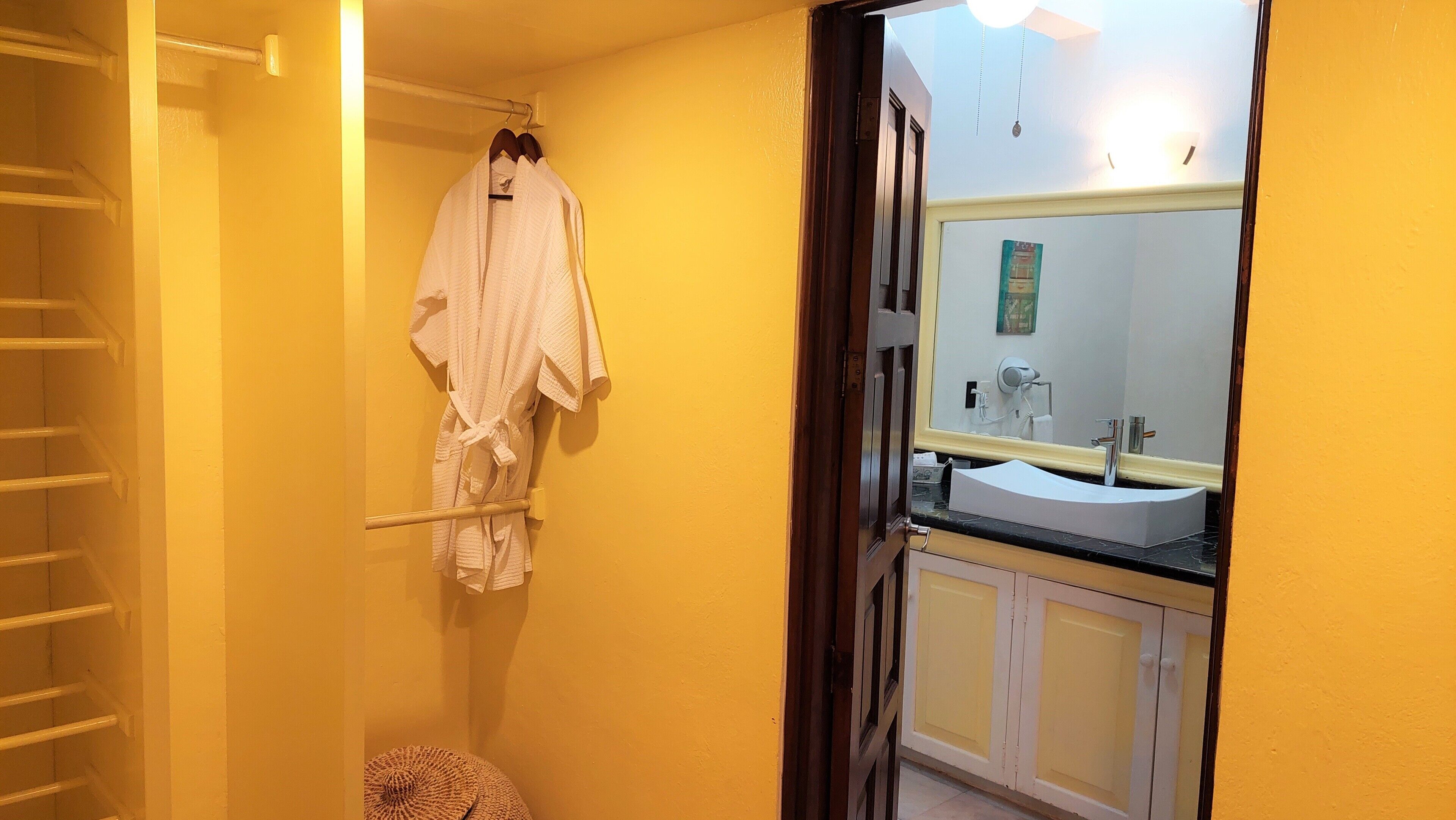 Een badkamer met een gele wand, een witte badkuip, een witte wastafel met een spiegel erboven en een handdoekrek met een witte handdoek.