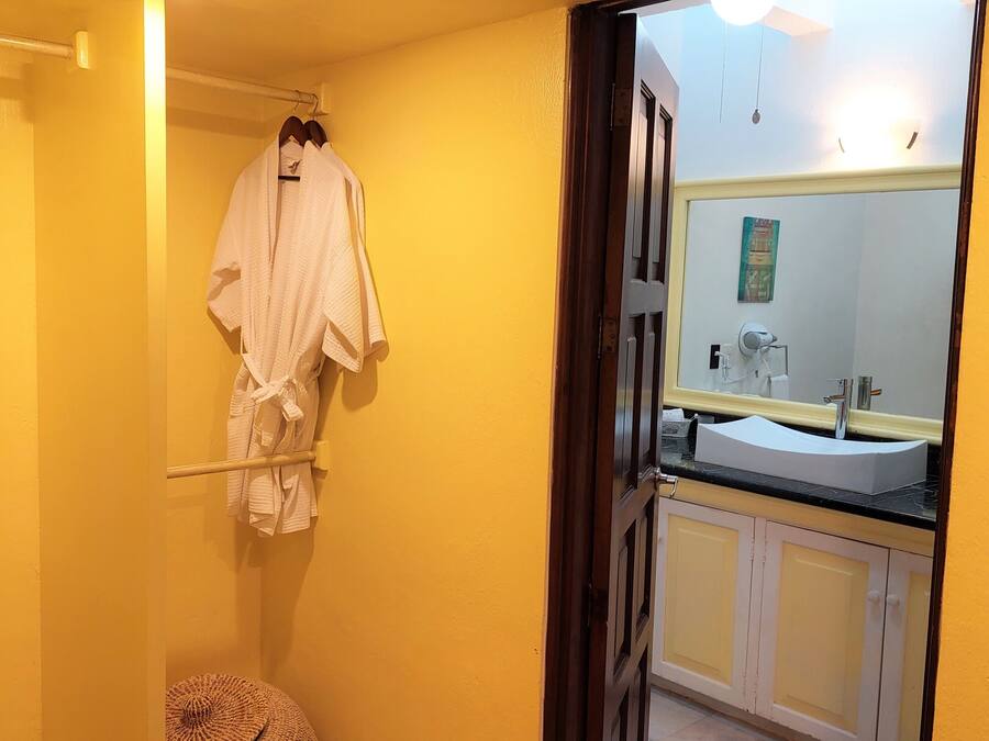 Een badkamer met een gele wand, een witte badkuip, een witte wastafel met een spiegel erboven en een handdoekrek met een witte handdoek.