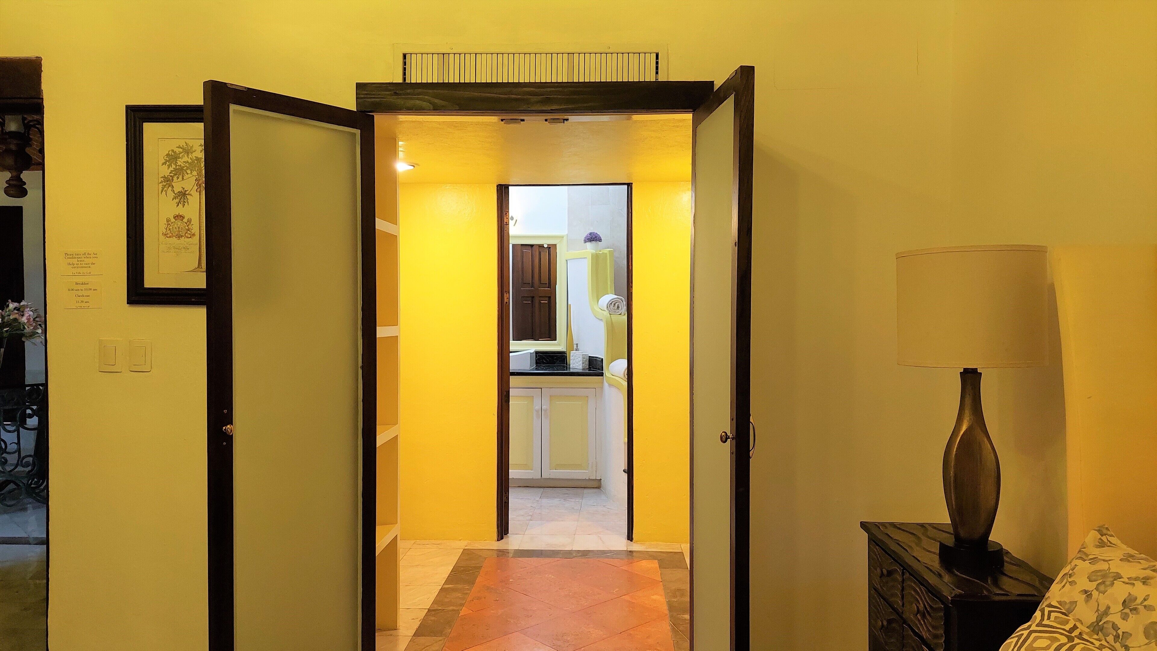 A hallway leading to a kitchen with a tiled floor, a lamp, and a framed picture on the wall.