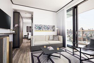 Une chambre d’hôtel moderne équipée d’un canapé, d’une table basse, d’une télévision et d’une grande fenêtre donnant sur la ville.
