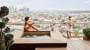 A couple on a rooftop terrace with a city view, a hot tub, and a potted plant. - The William Vale (Brooklyn)