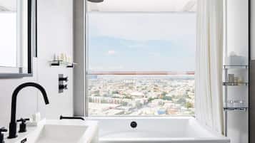 Une salle de bain moderne dotée d’une grande baignoire, d’une douche et offrant une vue sur la ville grâce à une grande fenêtre.