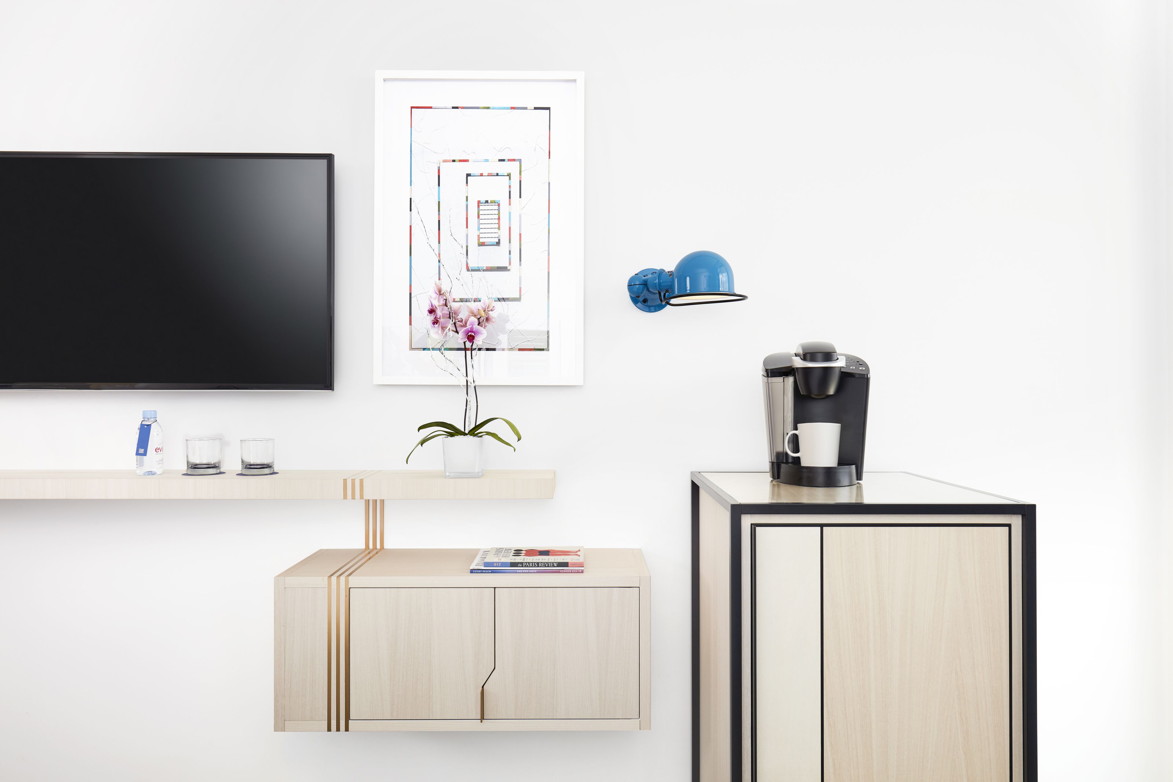 Habitación moderna con televisión de pantalla plana, una obra de arte abstracta enmarcada, cafetera y un mueble pequeño con una planta.