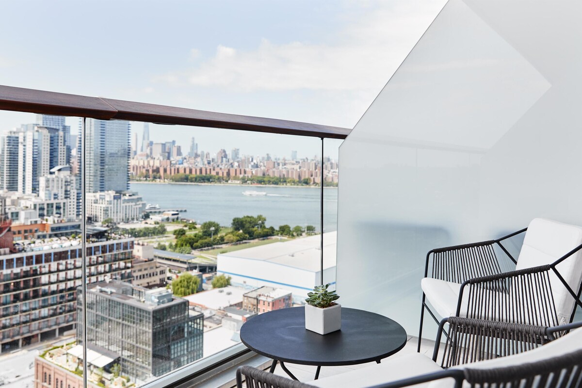 A balcony with a city view, a round table with a potted plant, and two wicker chairs.