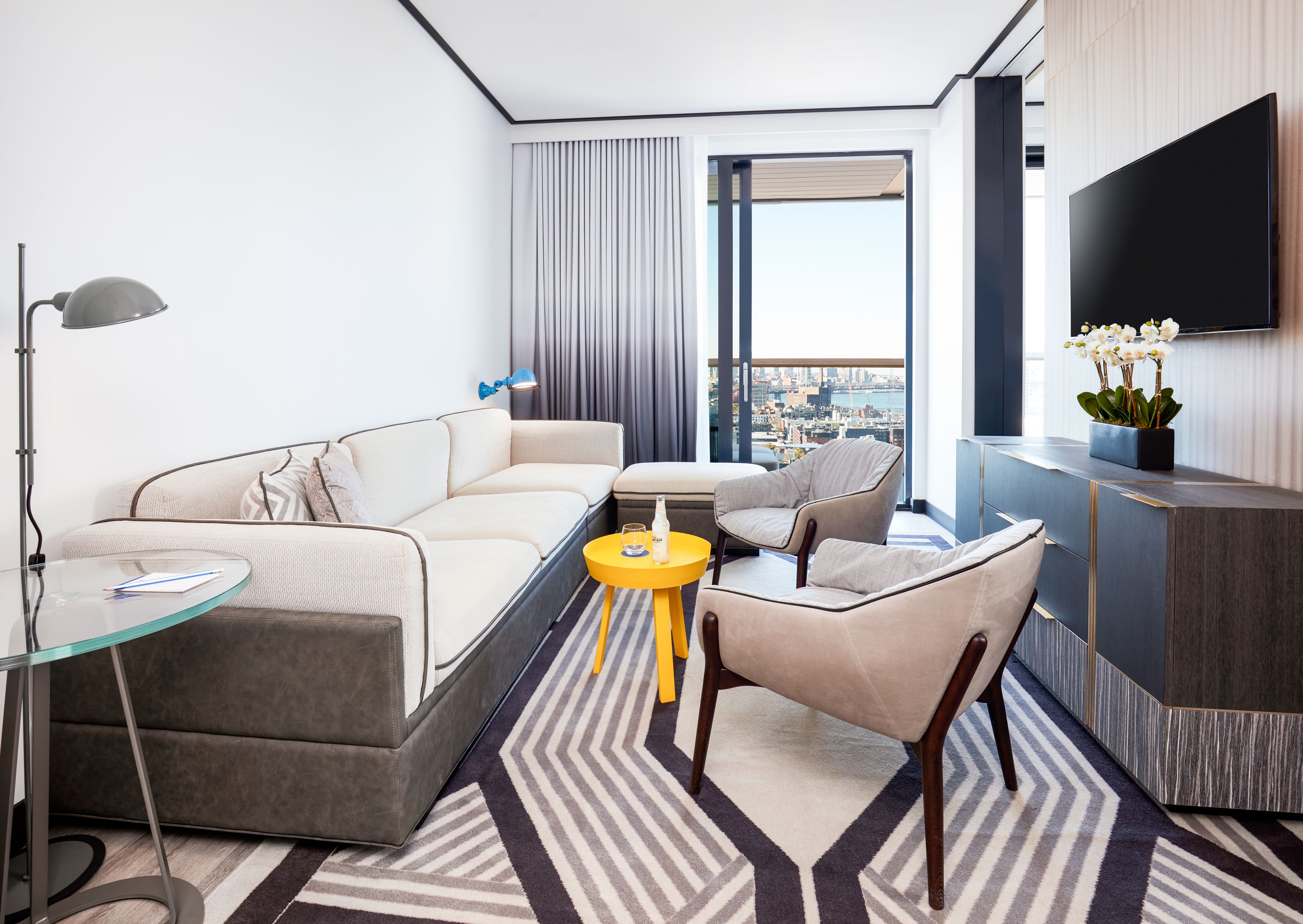 A modern hotel room with a sofa, armchair, and a small table.