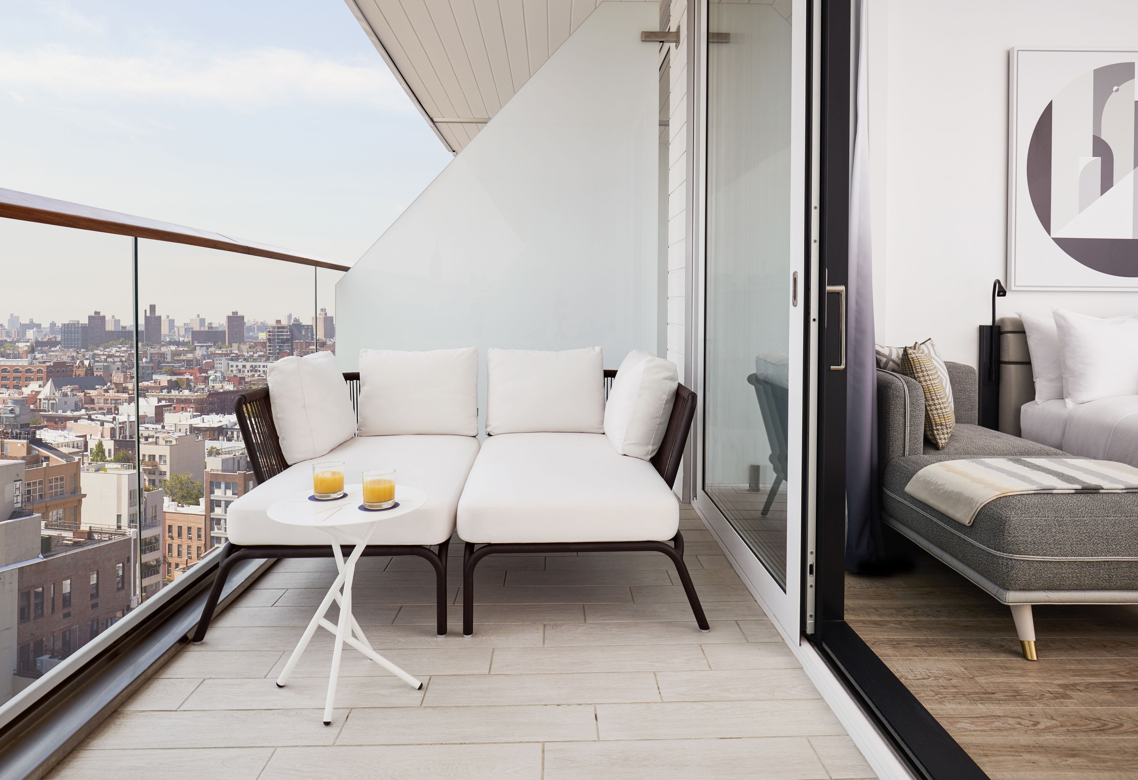 Ein Balkon mit Blick auf die Stadt, eine Sitzecke, ein kleiner Tisch mit Getränken und ein Bett.