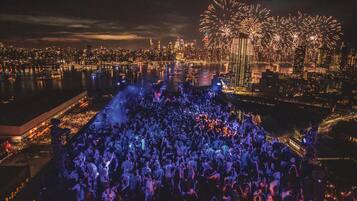 Ein belebtes Dachterrassen-Event mit Stadtansicht und Feuerwerk im Hintergrund.