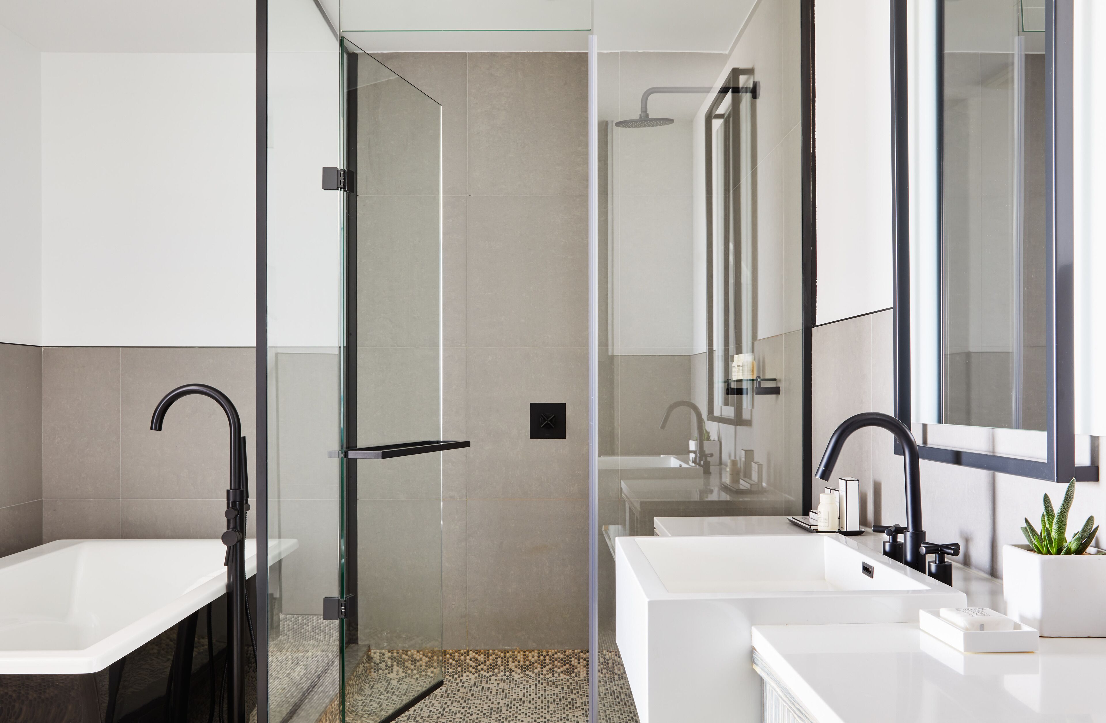 A modern bathroom with a glass-enclosed shower, two sinks, and a large mirror.