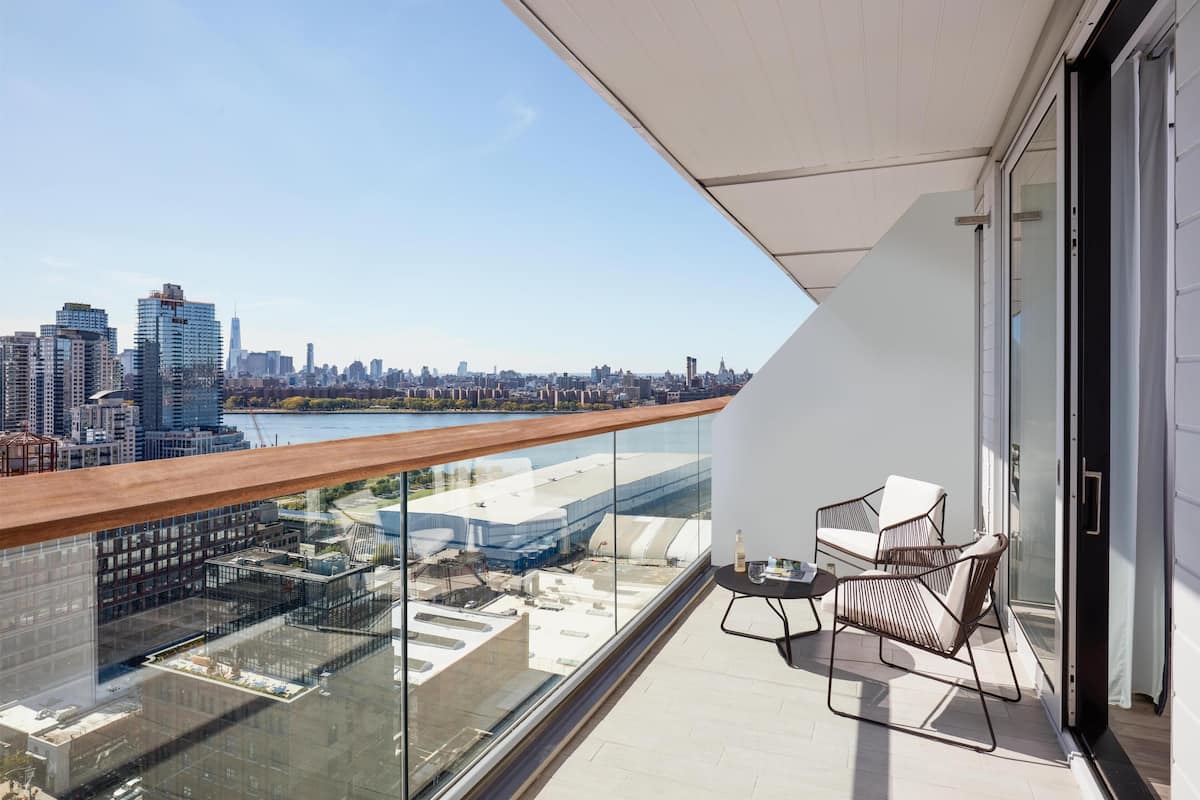 A balcony with a city view, a glass railing, and a seating area with chairs.