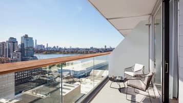 A balcony with a city view, a glass railing, and a seating area with chairs.