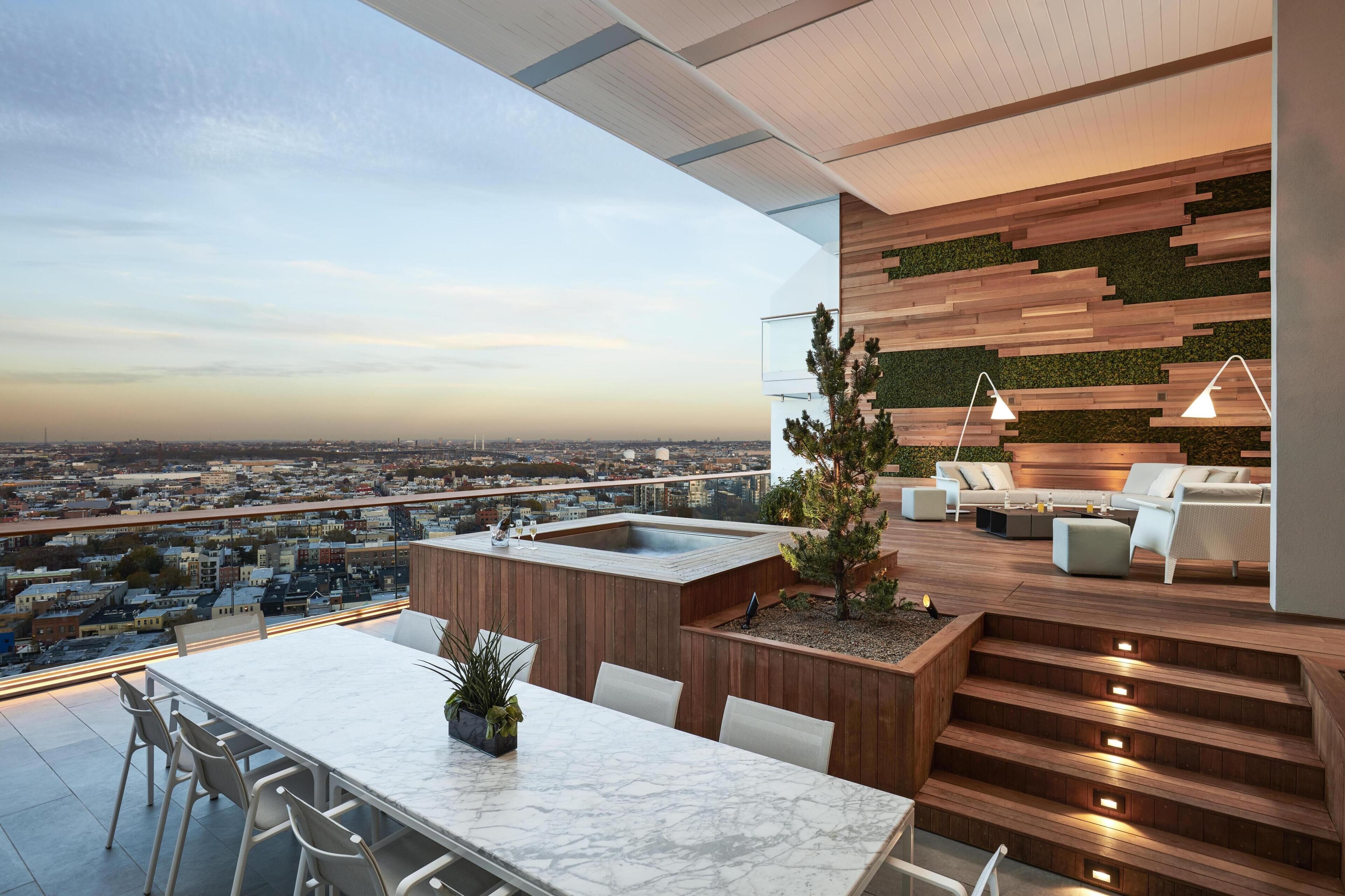 Terraza moderna en la azotea con vistas a la ciudad, zona de comedor y área de estar con pared de madera y detalles verdes.