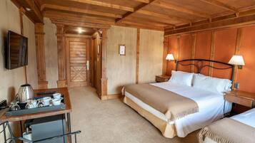 Quarto de hotel com teto de madeira, cama com roupa de cama branca, duas mesas de cabeceira com luminárias, escrivaninha com cafeteira e televisão na parede.