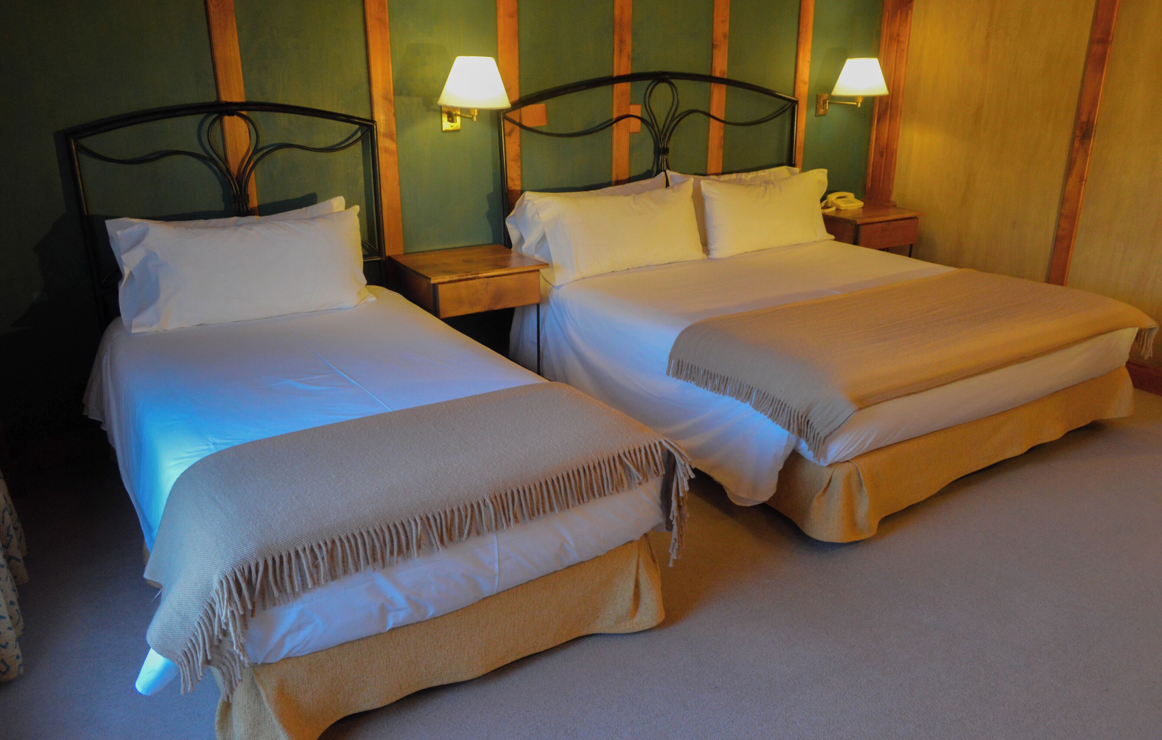 A hotel room with two beds, each with a headboard, bedside tables, lamps, and a carpeted floor.