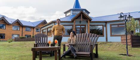 Una cabaña de madera con techo azul y una torre cónica, una banca de madera, y una mesa con una bebida.