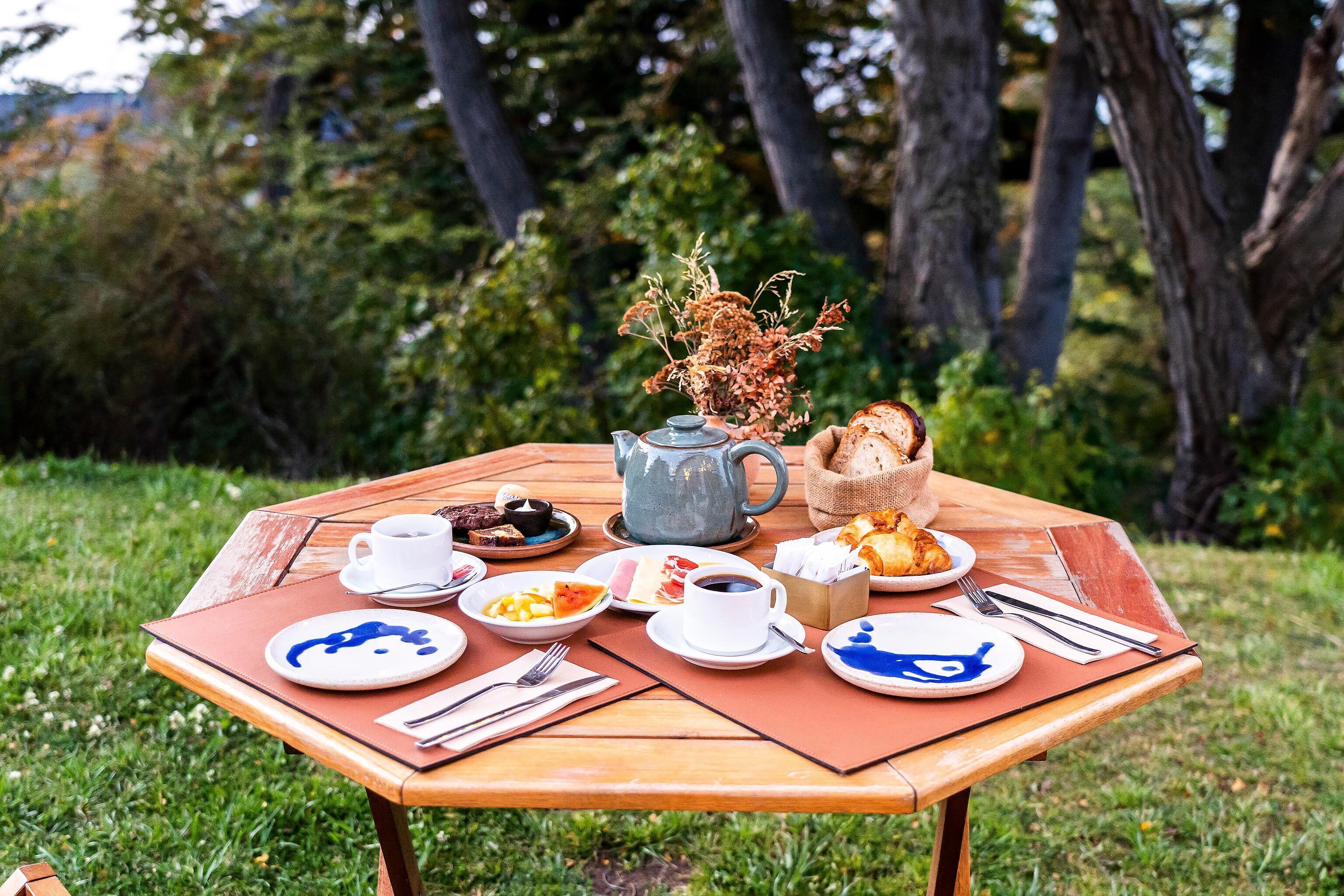 An outdoor dining table with various dishes, a teapot, and a vase of dried flowers.