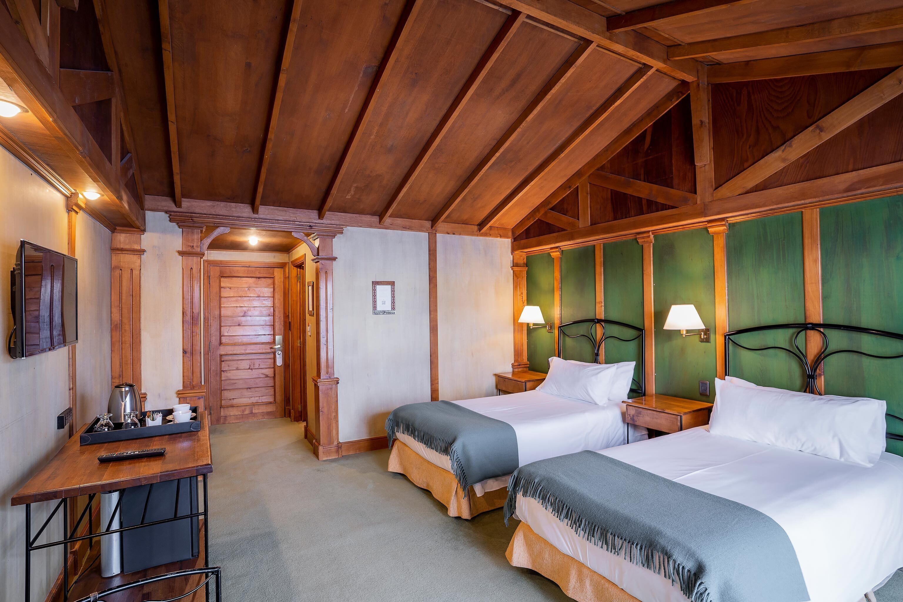 A hotel room with two beds, a desk with a kettle, and a green accent wall.