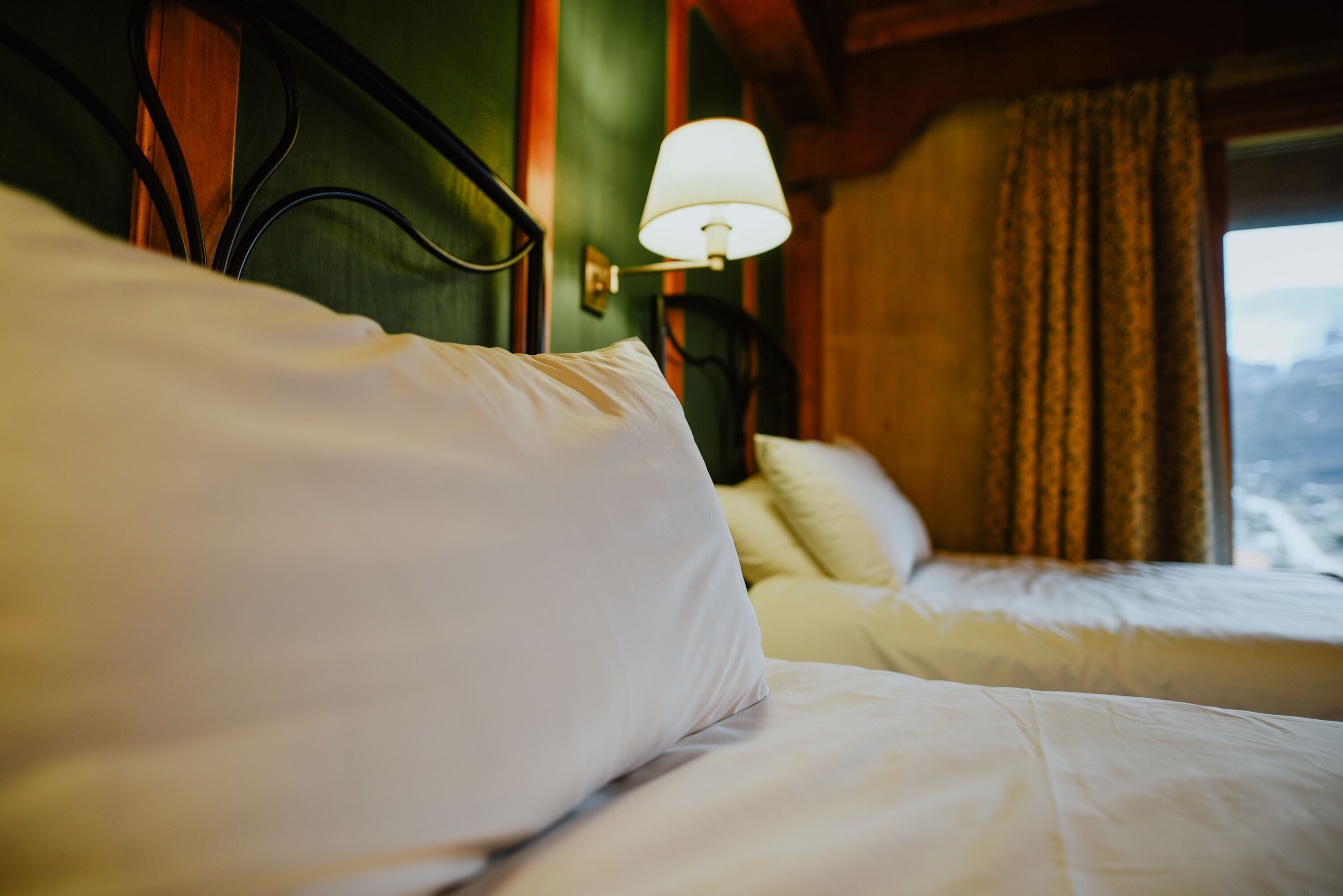 Une chambre d’hôtel avec deux lits, une lampe et une fenêtre avec des rideaux.