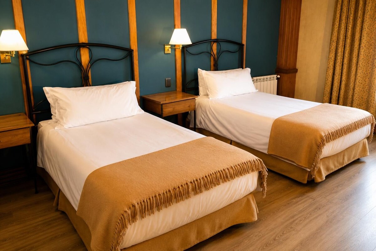 Habitación de hotel con dos camas individuales, cabeceros de madera, mesitas de noche con lámparas y suelo de madera.