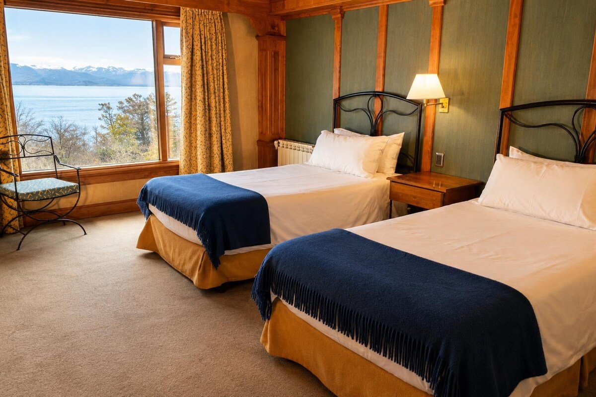 Habitación de hotel con dos camas, vista a un lago, una silla y una lámpara.