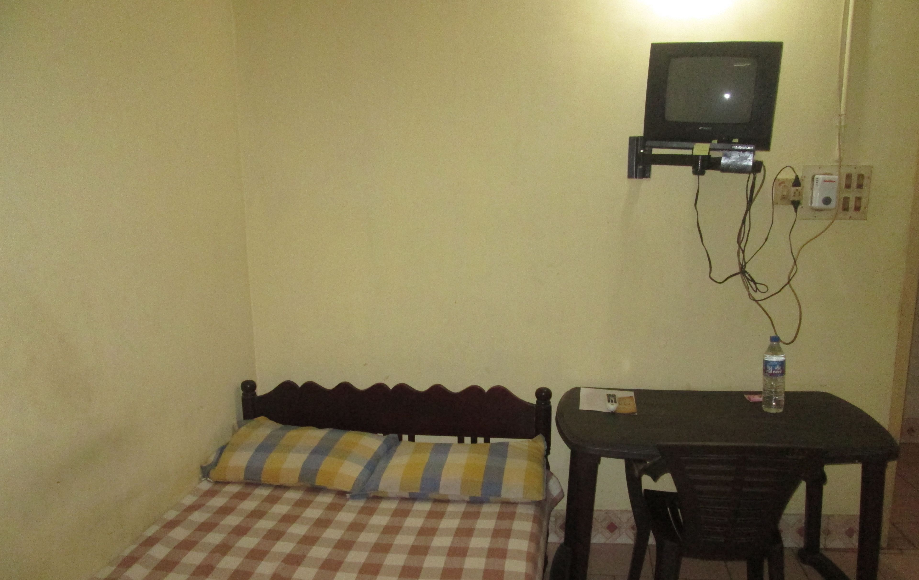 A small room with a bed, a table, a chair, a television mounted on the wall, and a water bottle on the table.