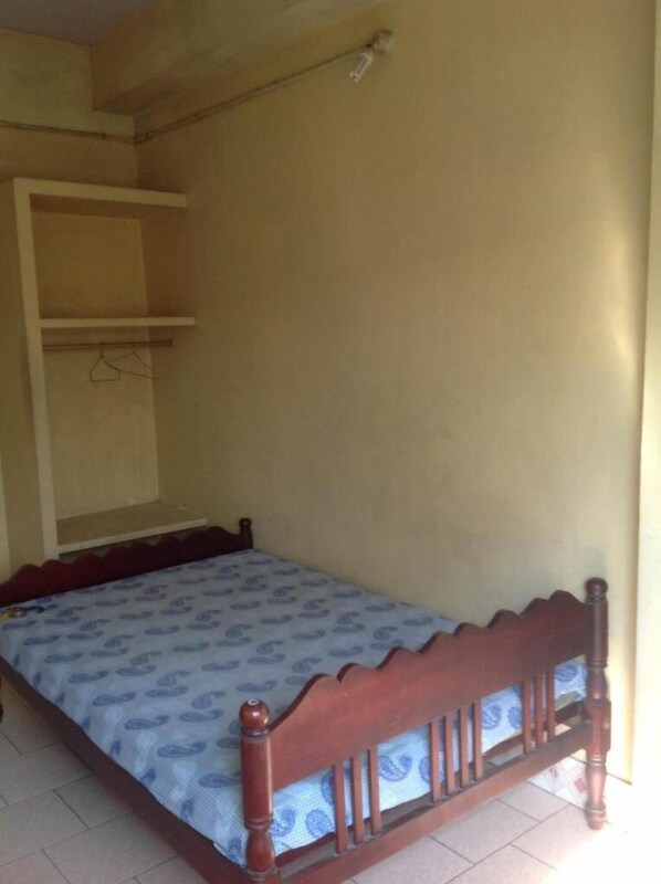 Un dormitorio con una cama individual, cabecera de madera, armario y suelo de baldosas.