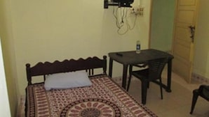 A small room with a bed, a table, a chair, and a television mounted on the wall. - St.Antonys Lodge Ernakulam Market (Kanayannur)